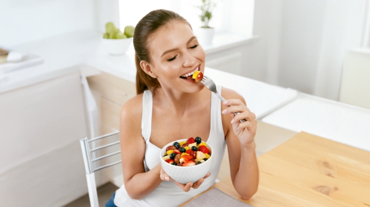 Smiling woman enjoying a fresh fruit salad, highlighting healthy eating tips for maintaining oral health during the holidays in Tempe, AZ.